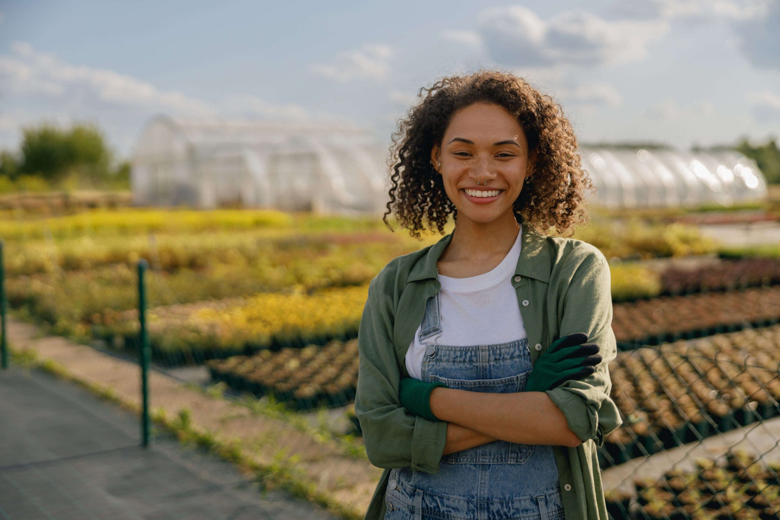 Professional smiling female farmer standing on the field on greenhouses background